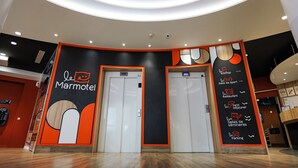Un intérieur moderne avec deux ascenseurs, une enseigne indiquant « Le Marmotel », et un panneau répertoriant les différents services proposés, tels qu’un restaurant et un parking.