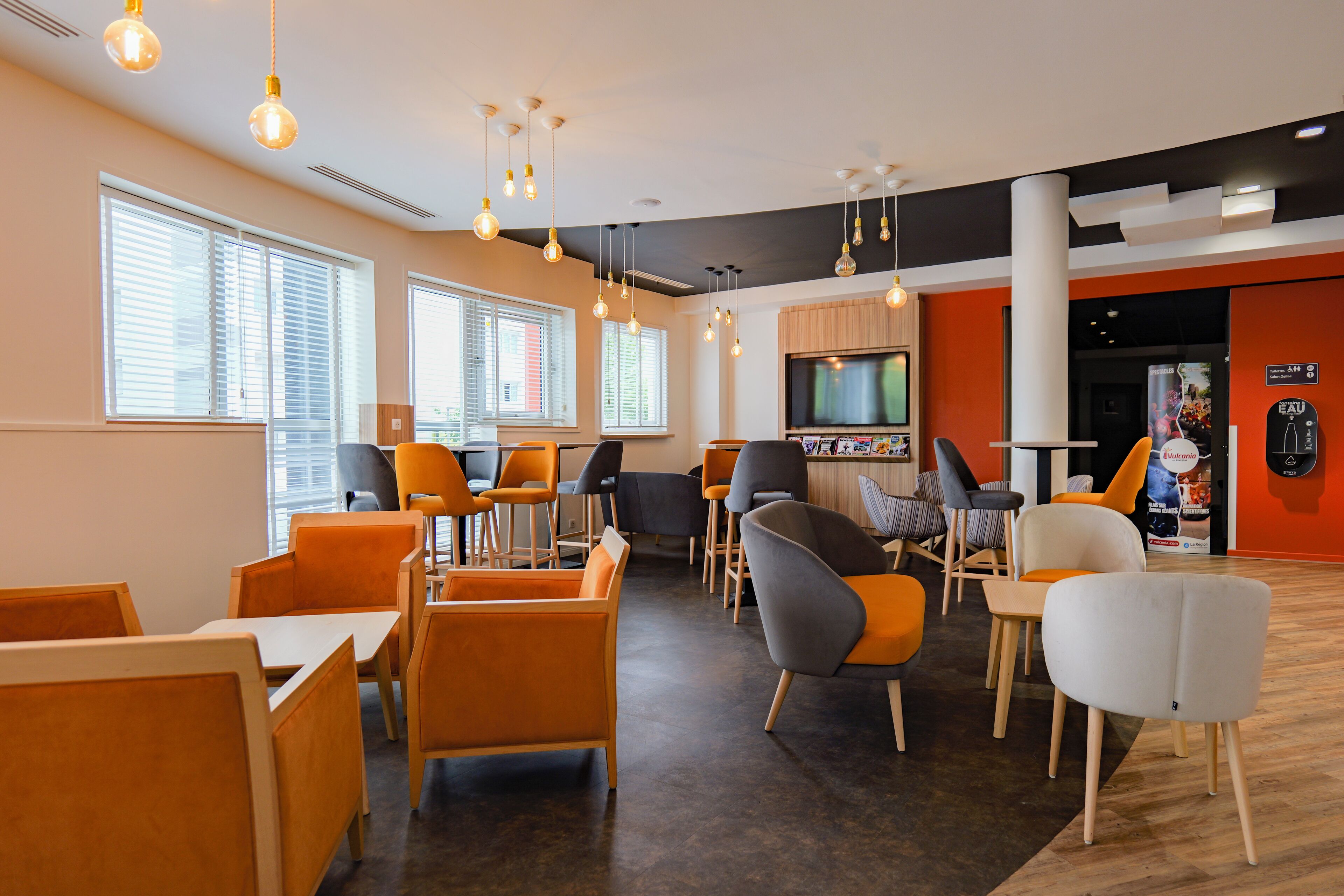 A modern indoor space with multiple seating areas, including tables and chairs, and a television screen.