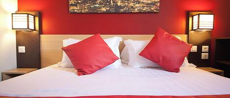 Una habitación de hotel con una cama grande, almohadas rojas y dos lámparas fijadas a la pared.