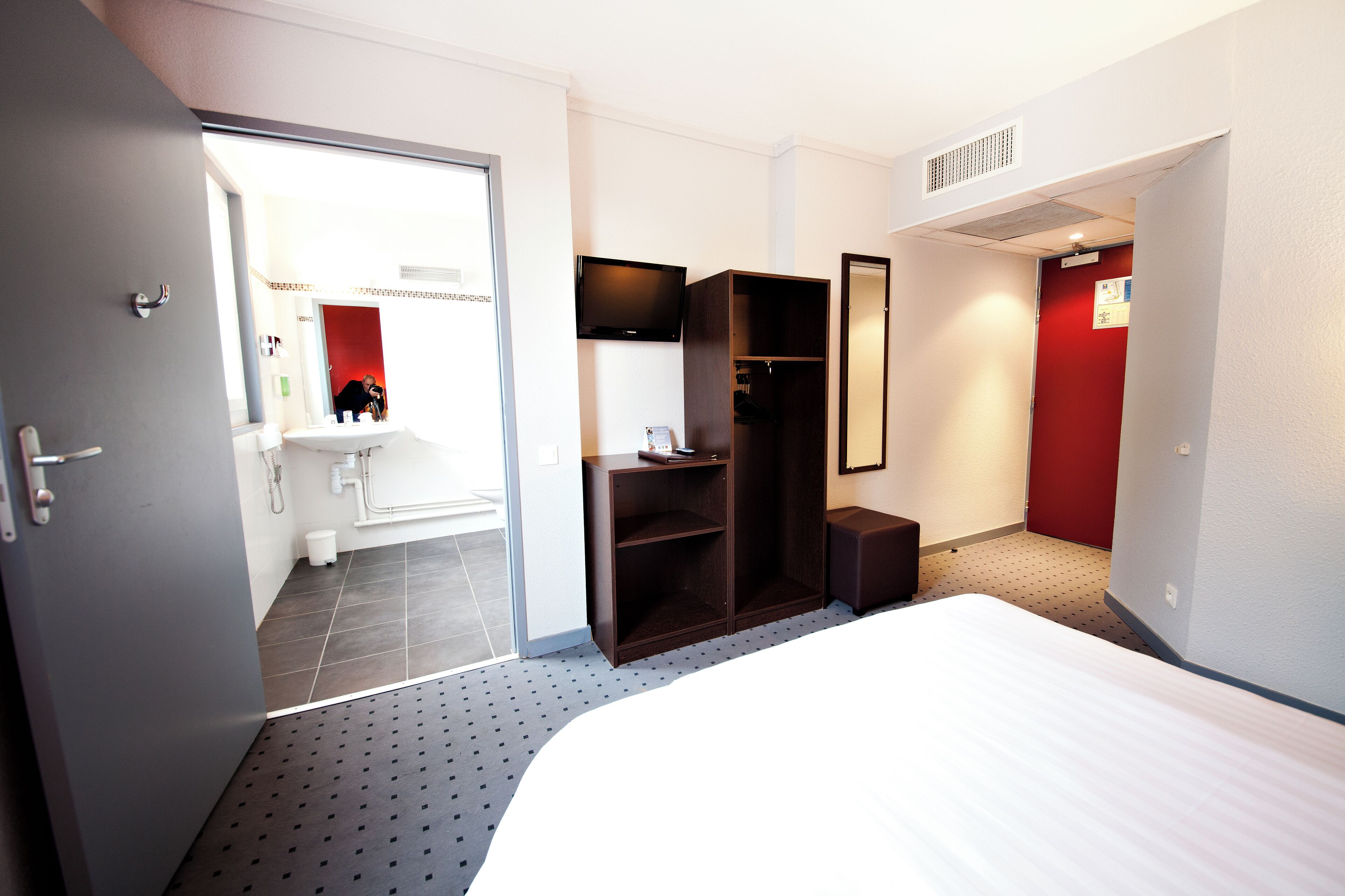 A hotel room with a bed, a wardrobe, a mirror, and a television.