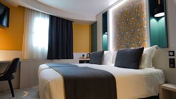 Habitación de hotel con una cama grande, un escritorio, una silla, un televisor y un papel tapiz estampado.