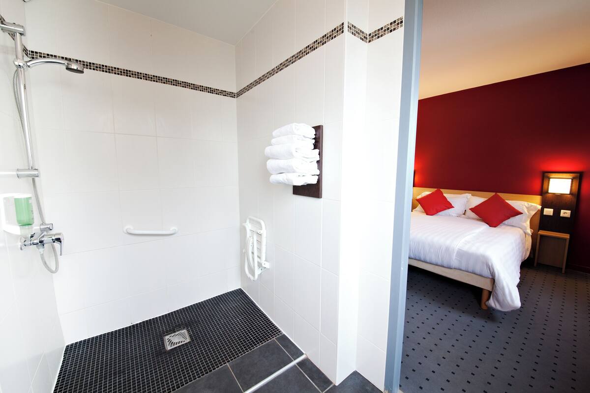 Une salle de bain d’hôtel avec une douche, un porte-serviettes et un lit dans la pièce adjacente.