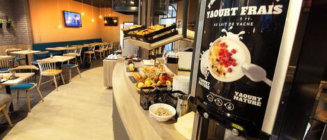 A café with a buffet-style breakfast setup, a coffee machine, and a TV mounted on the wall.