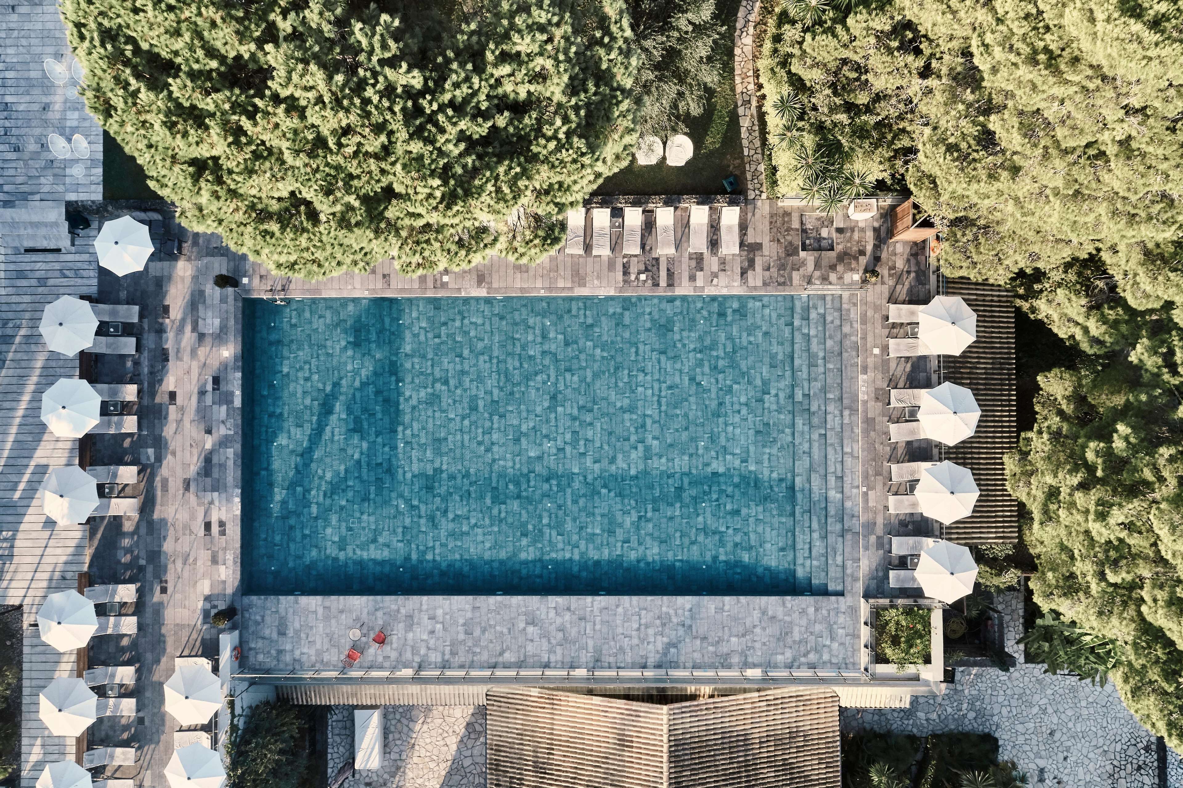 An aerial view of a rectangular swimming pool with surrounding lounge areas, stone pathways, and lush greenery.