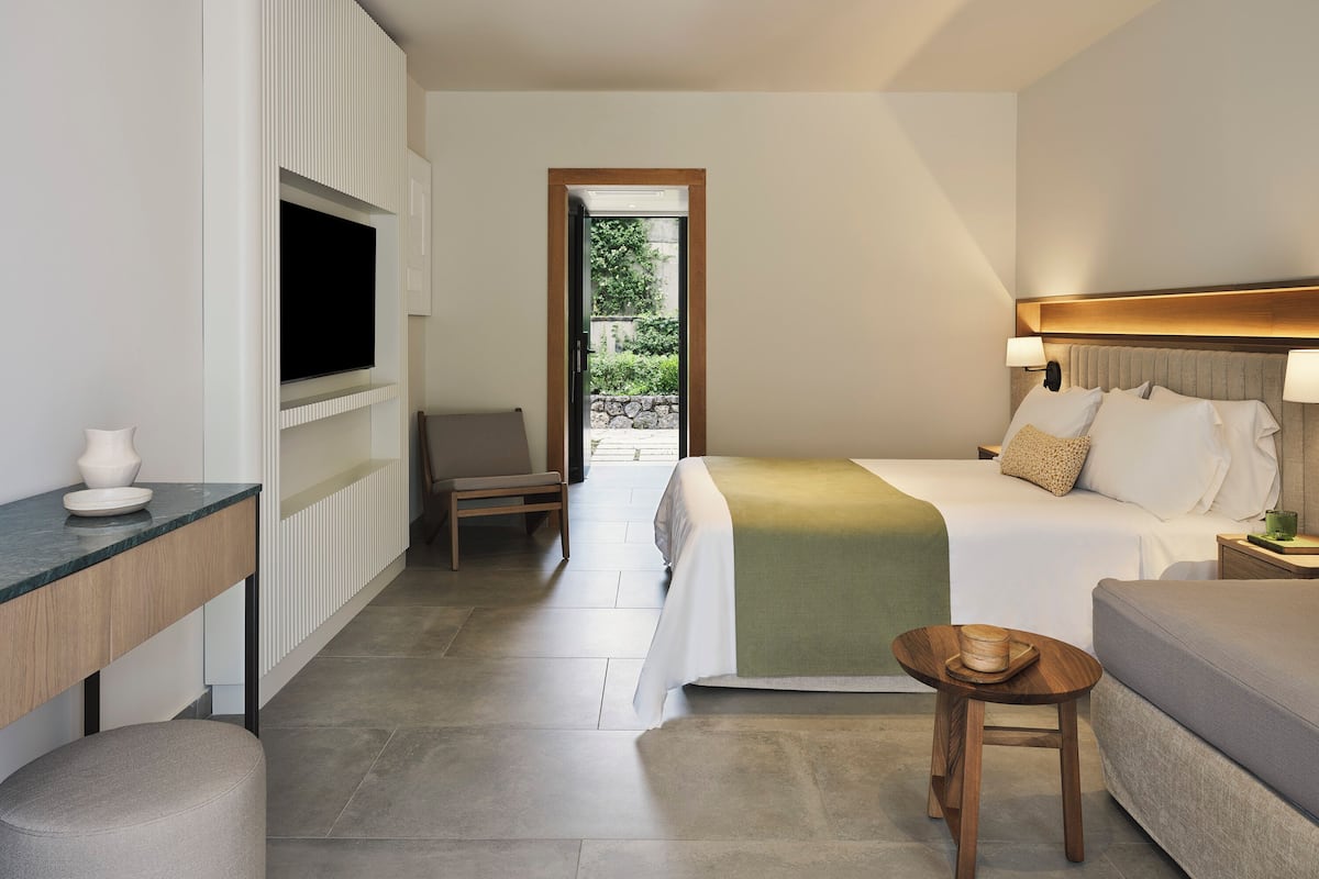 A modern hotel room with a bed, a sofa, a small table, a chair, and a TV.