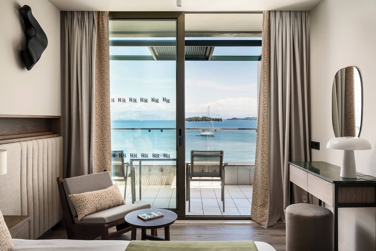 A hotel room with a balcony, a sofa, a chair, a small table, and a mirror.