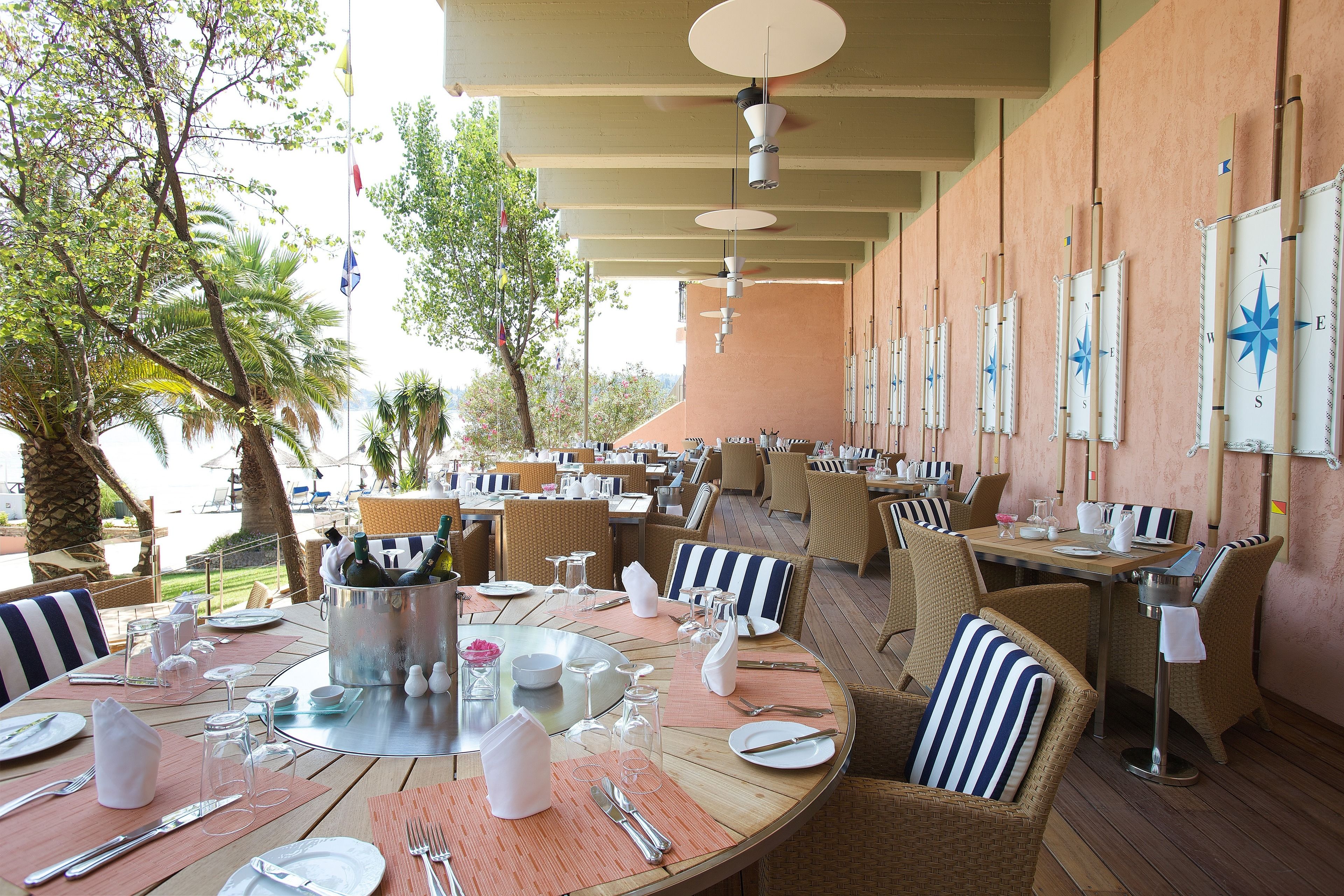 An outdoor dining area with round tables, wicker chairs, and a view of the sea.