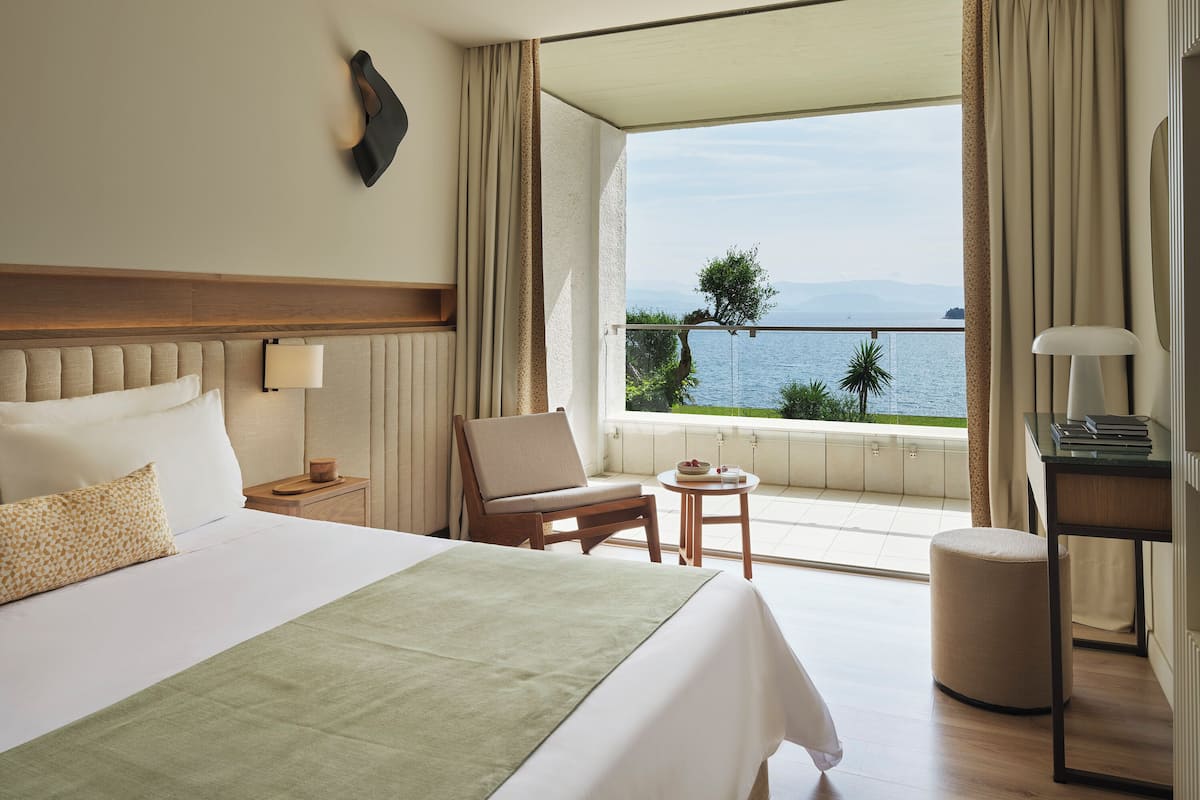 A hotel room with a large bed, a chair, a small table, and a view of the sea.