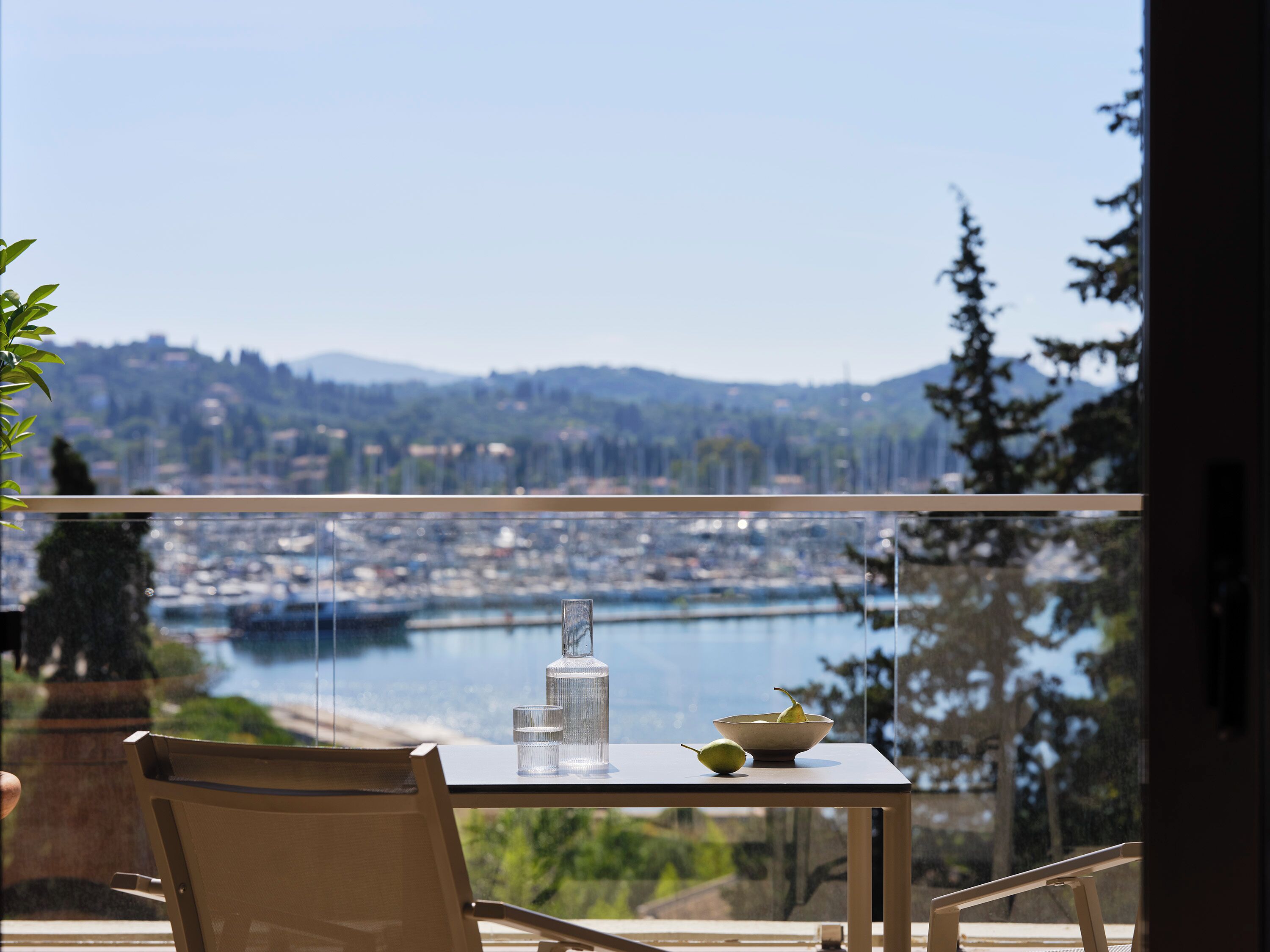 Una mesa con una botella y un cuenco en un balcón con vistas a un puerto deportivo y al paisaje urbano.