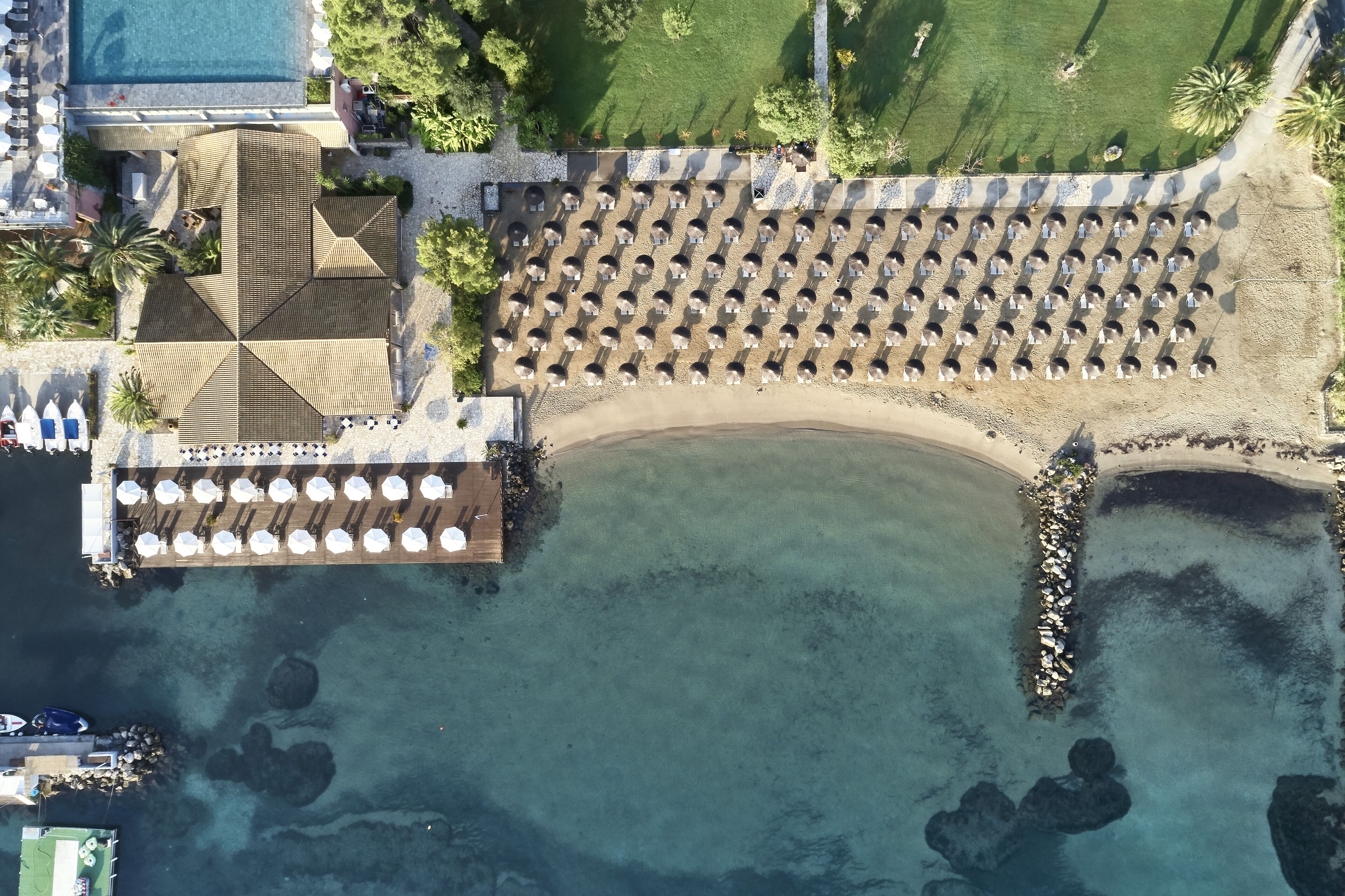 An aerial view of a resort with a beach area, a pool, and a dining area with umbrellas.