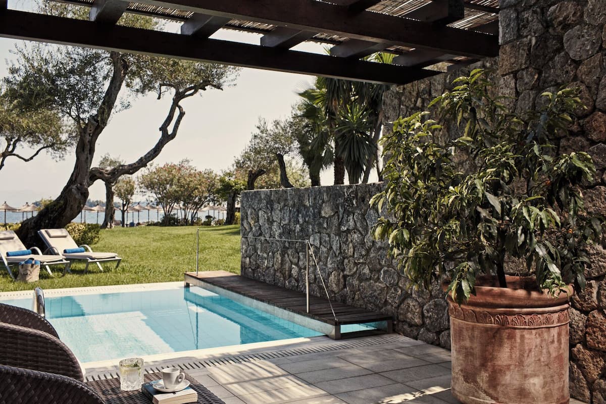 A pool area with a stone wall, lounge chairs, and a potted plant.