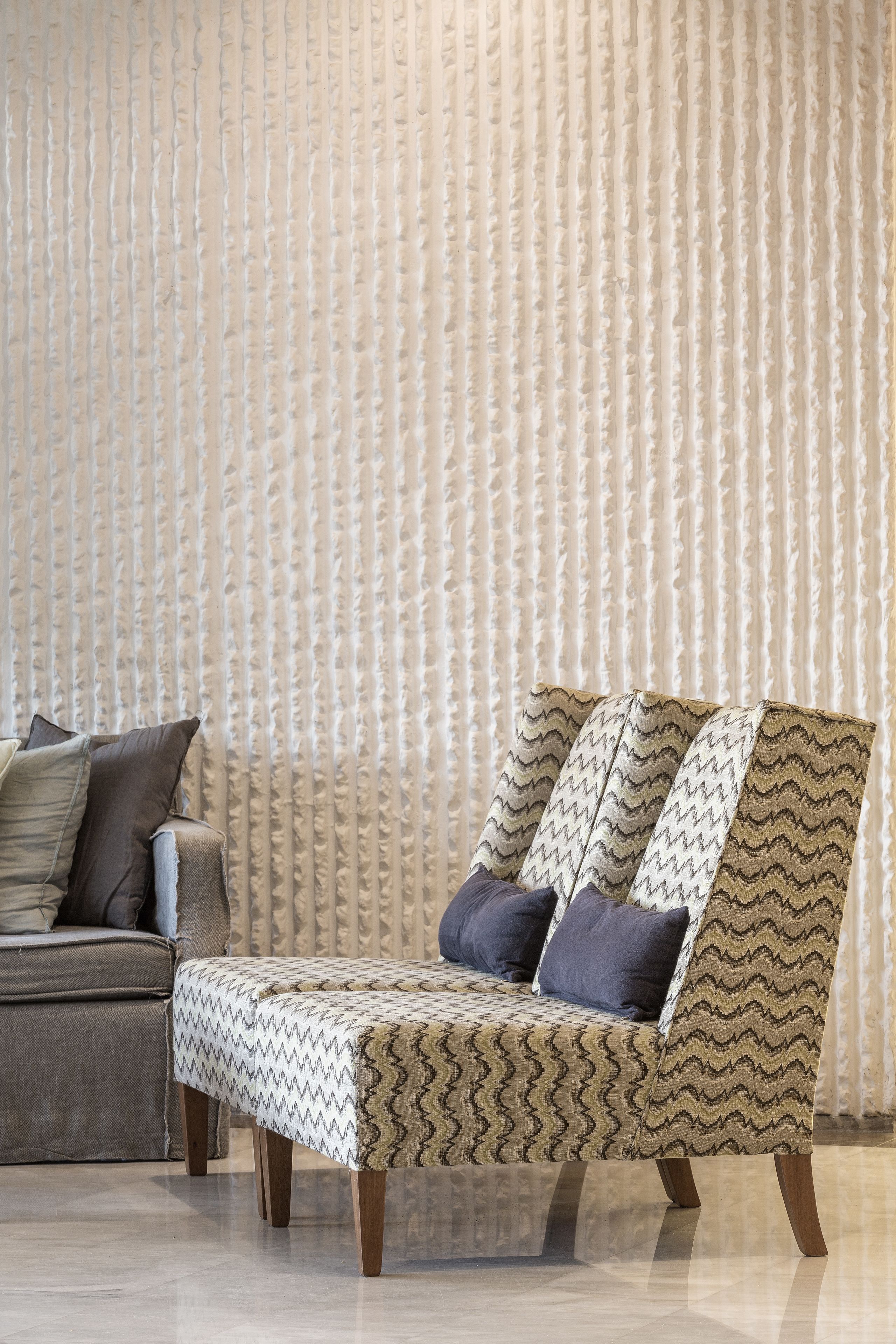 Una sala moderna con un sillón estampado, un sofá y una pared con textura.