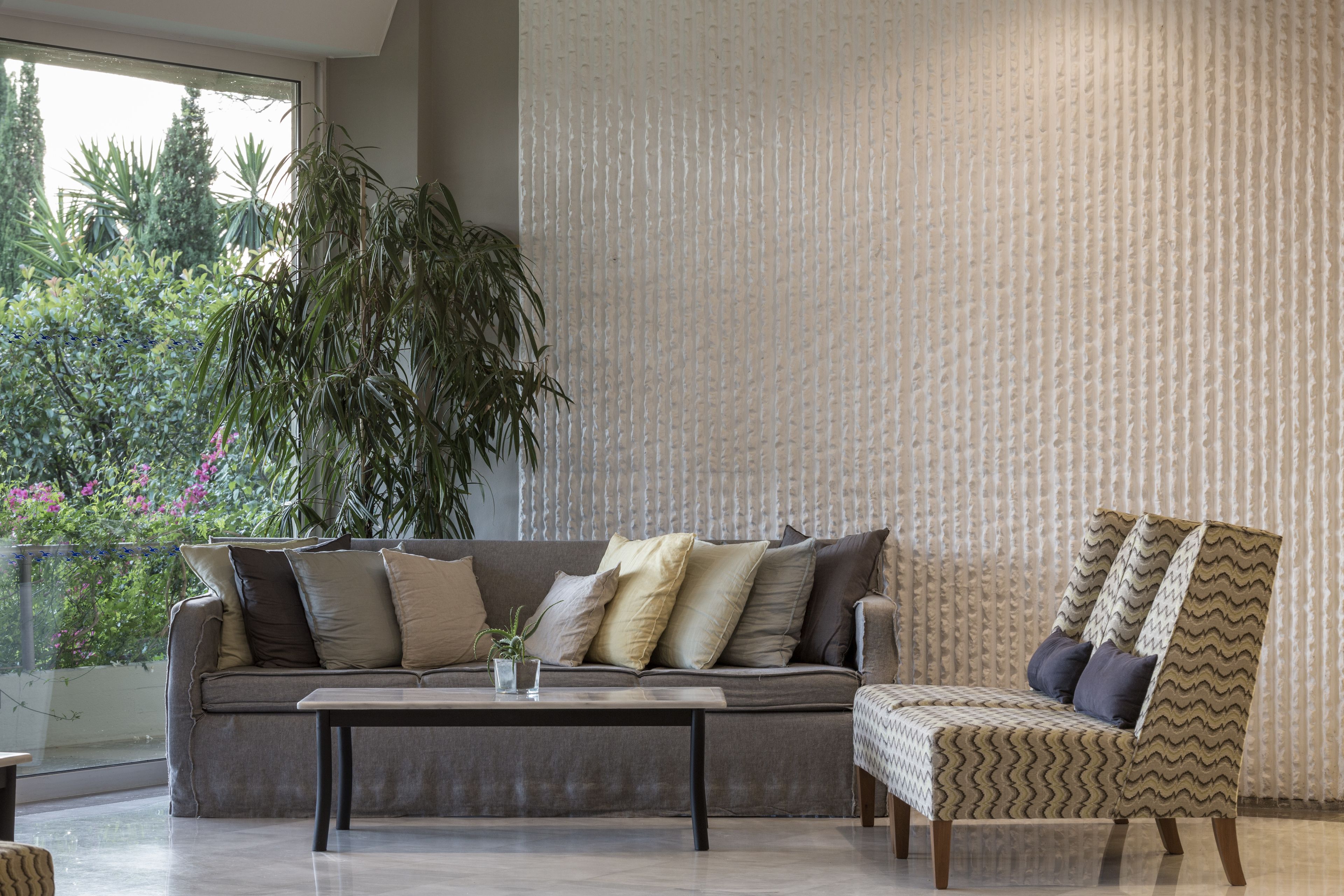 A modern living room with a sofa, a patterned armchair, a coffee table, and a large potted plant.