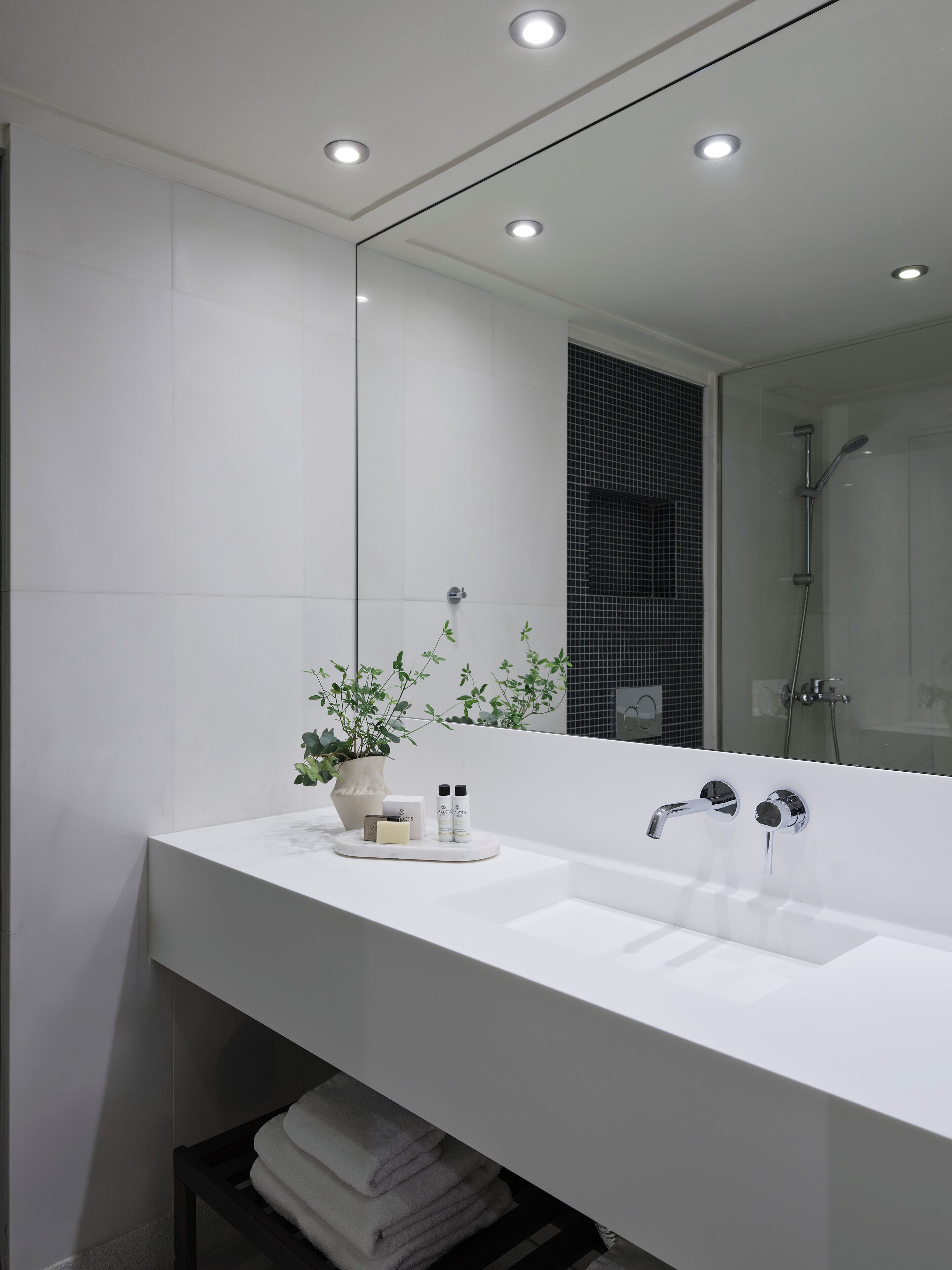 Un baño moderno con un tocador blanco, un espejo grande y una zona de ducha.