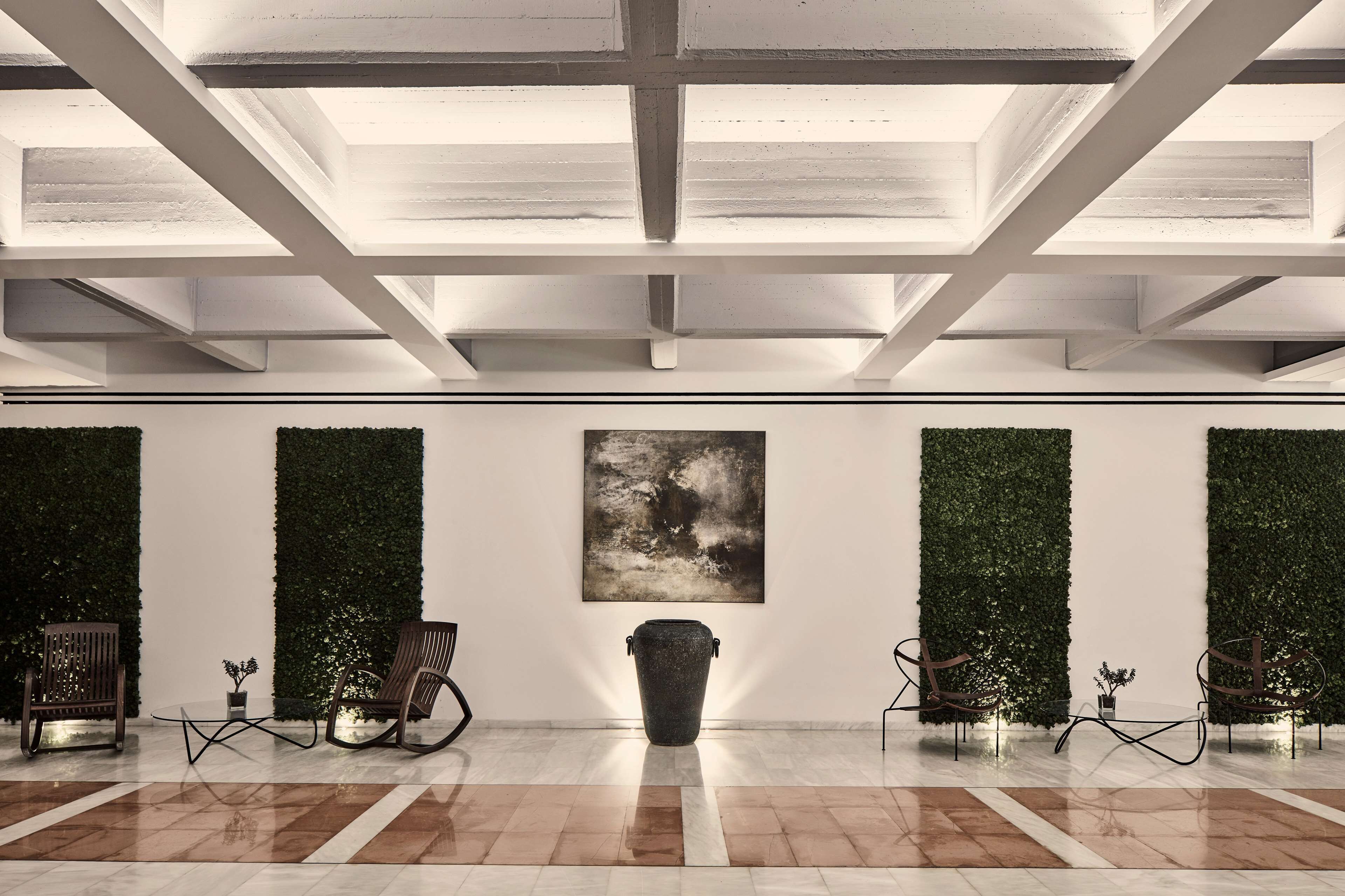 Un hall d’entrée spacieux avec un plafond haut, un espace de détente central avec des fauteuils et une table, et une grande peinture abstraite accrochée au mur.