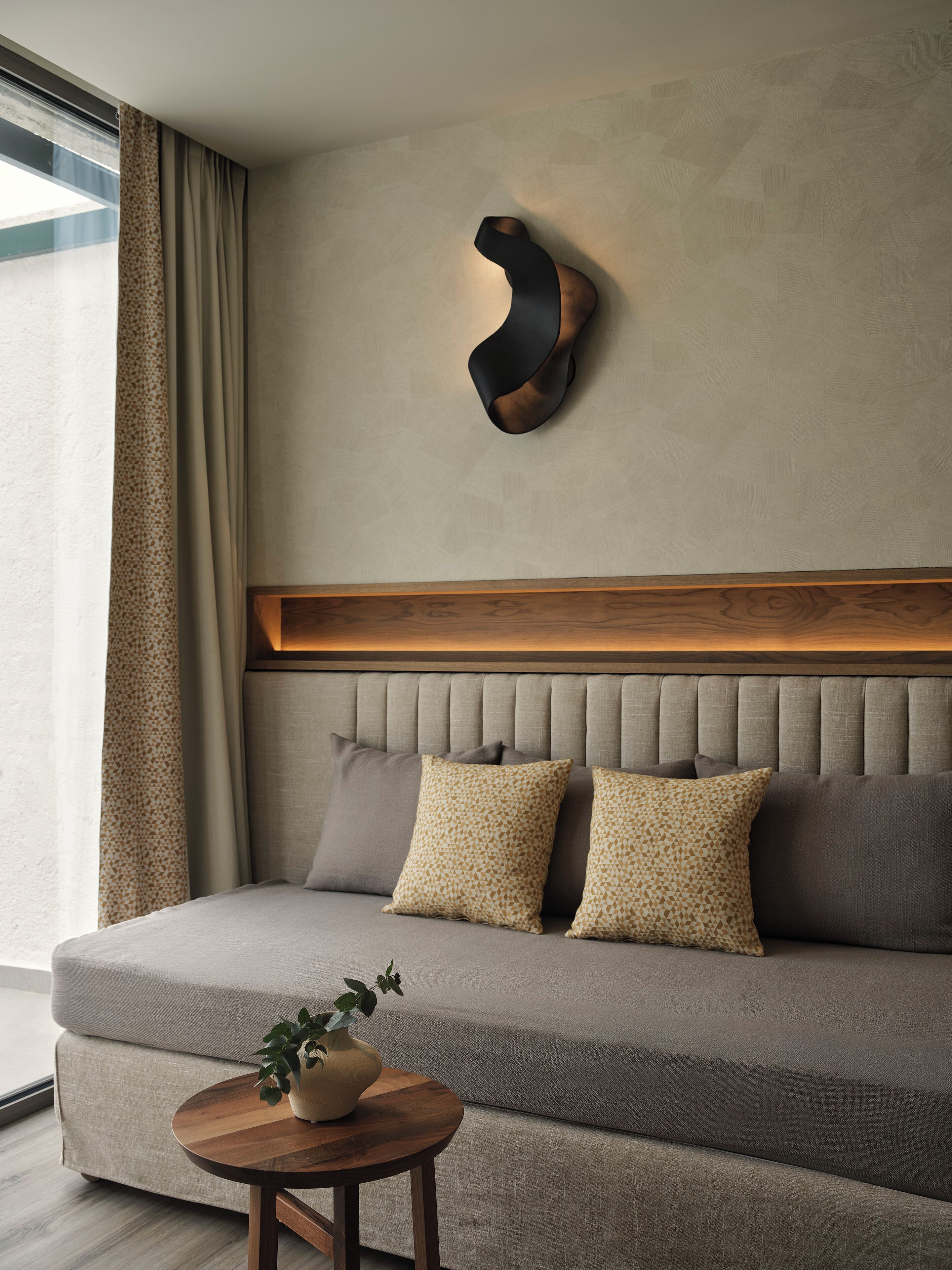 Ein modernes Wohnzimmer mit einer Couch, Kissen, einem Holztisch und einer Wandleuchte.