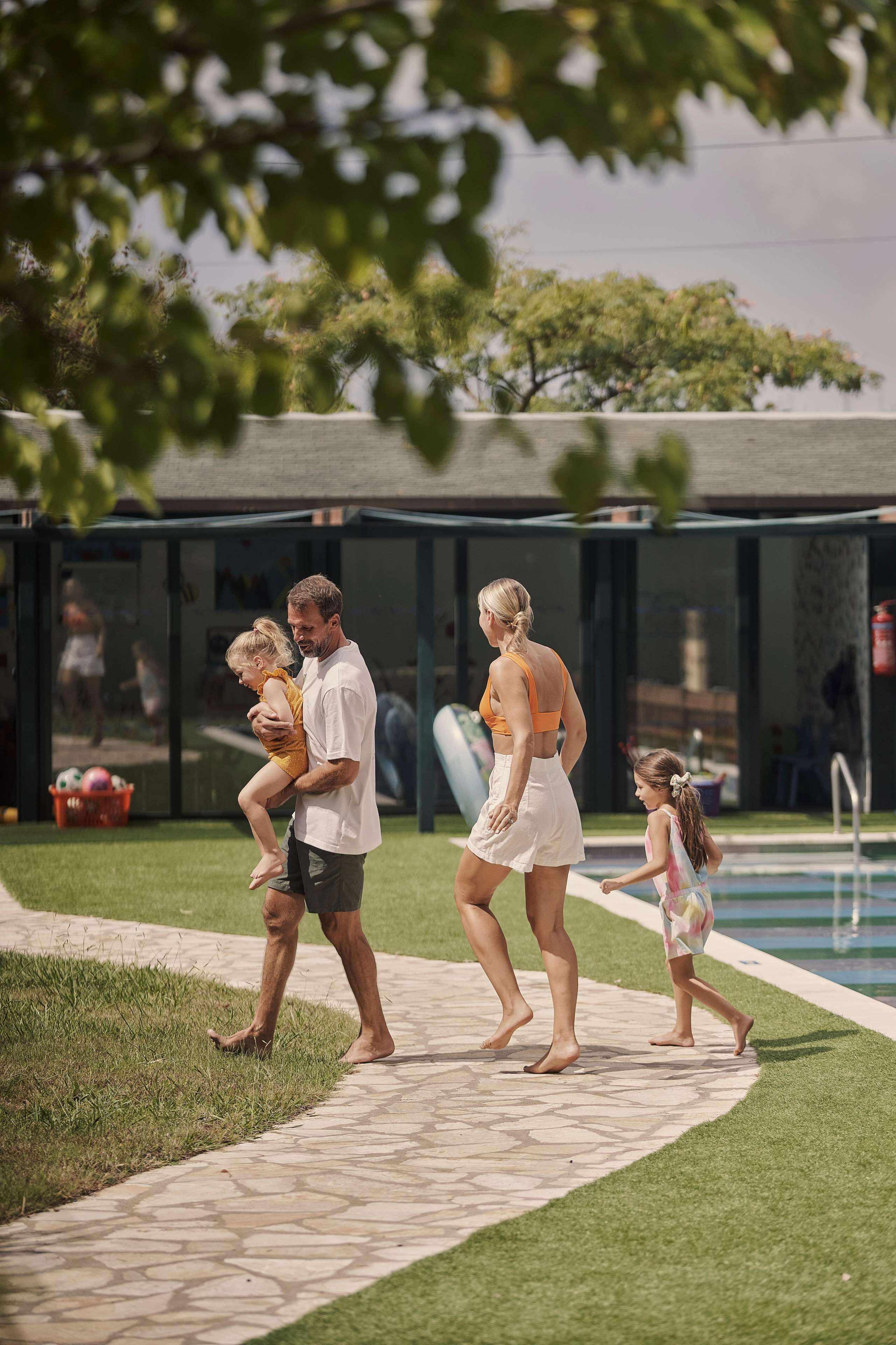 A family walking along a pathway beside a pool, with a building in the background.