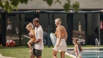 A family walking along a pathway beside a pool, with a building in the background.