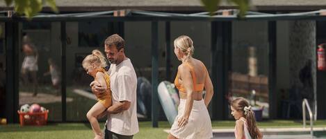 A family walking along a pathway beside a pool, with a building in the background.