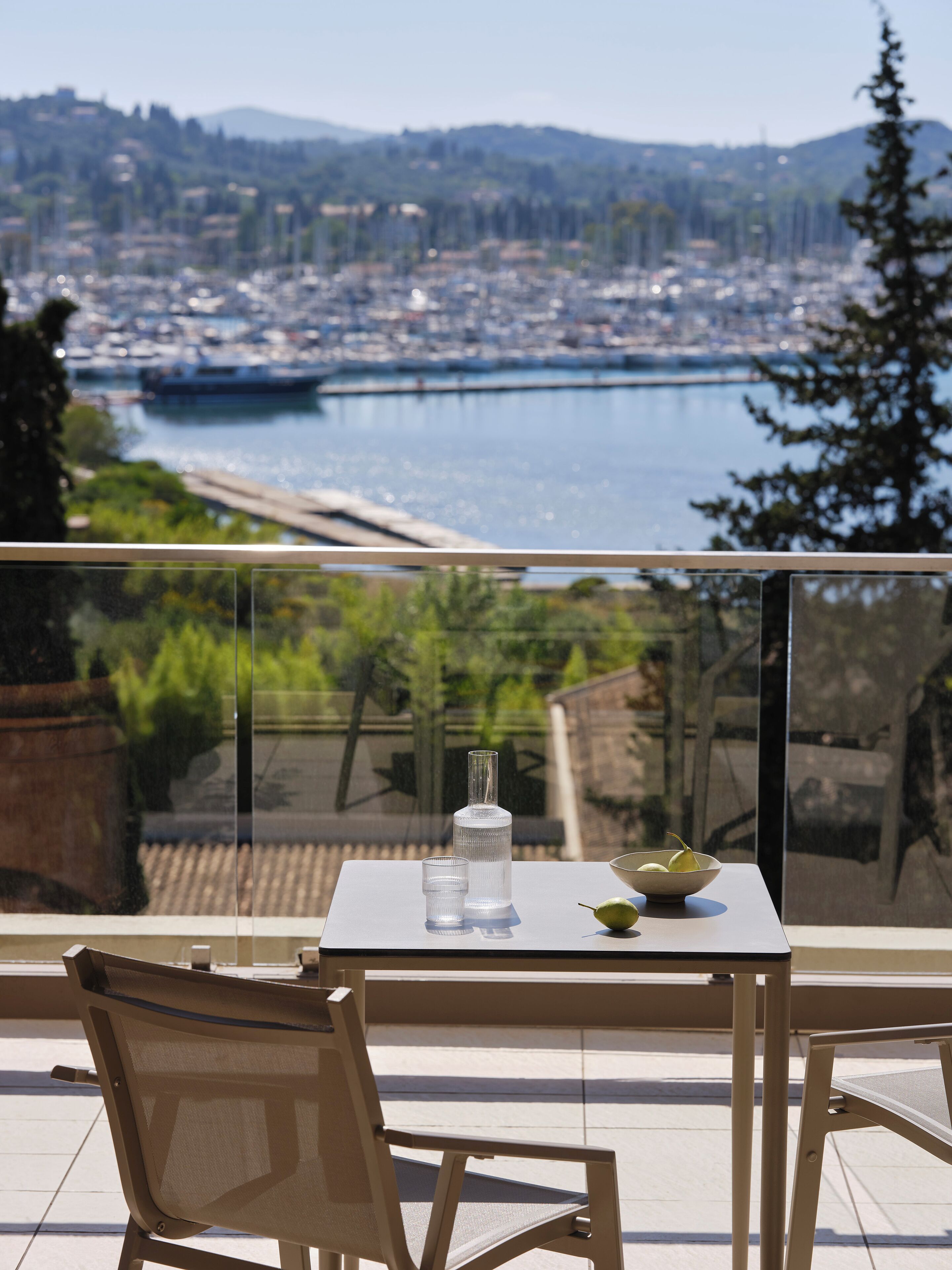 A balcony with a table, chairs, and a view of a cityscape and water body.