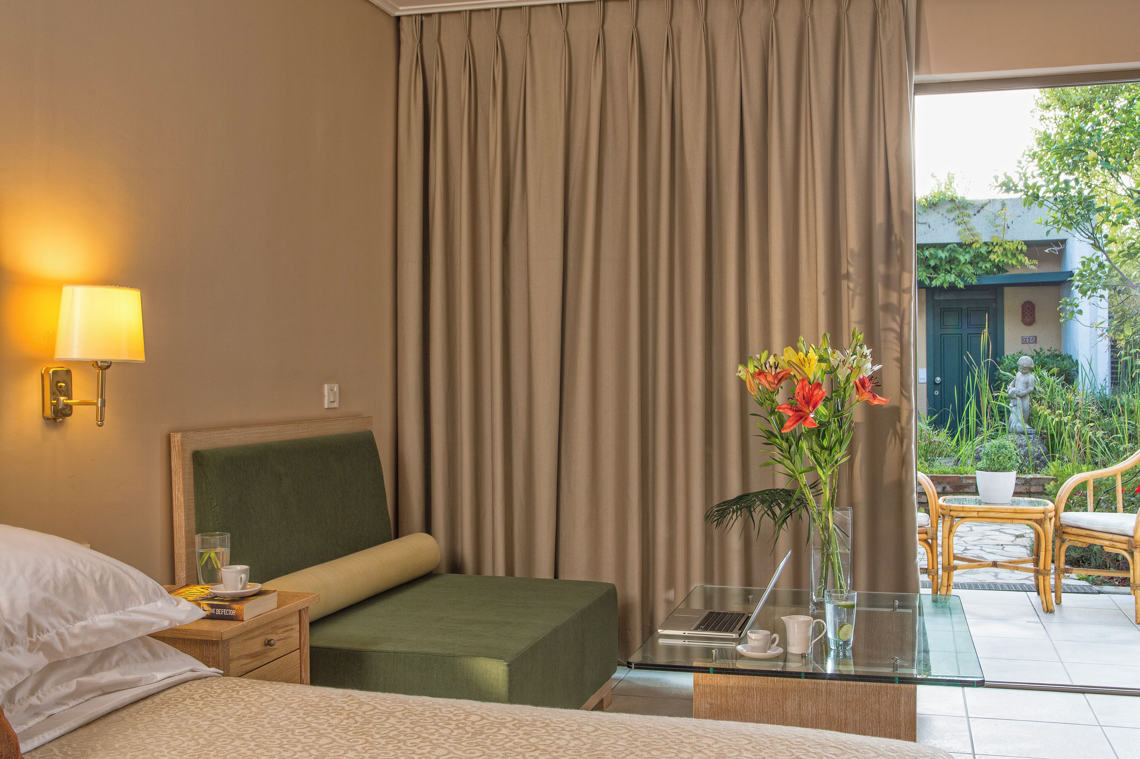 A hotel room with a bed, bedside table, lamp, and a view of the garden.