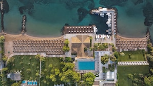 Vista aérea de un resort con una piscina grande, varias zonas de estar en la playa y un muelle con barcos.