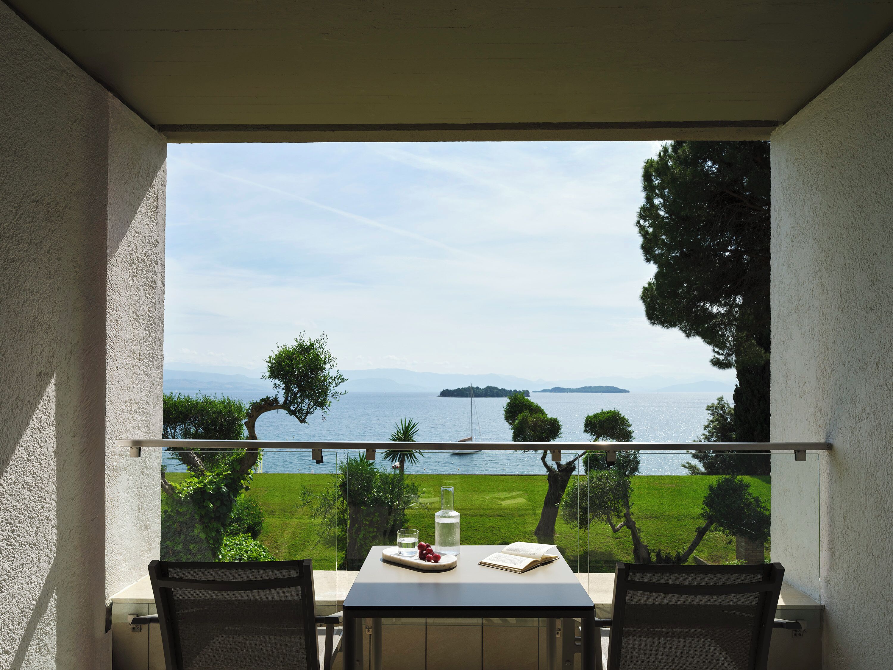 Un balcone con tavolo, sedie e vista sul mare e sul verde.