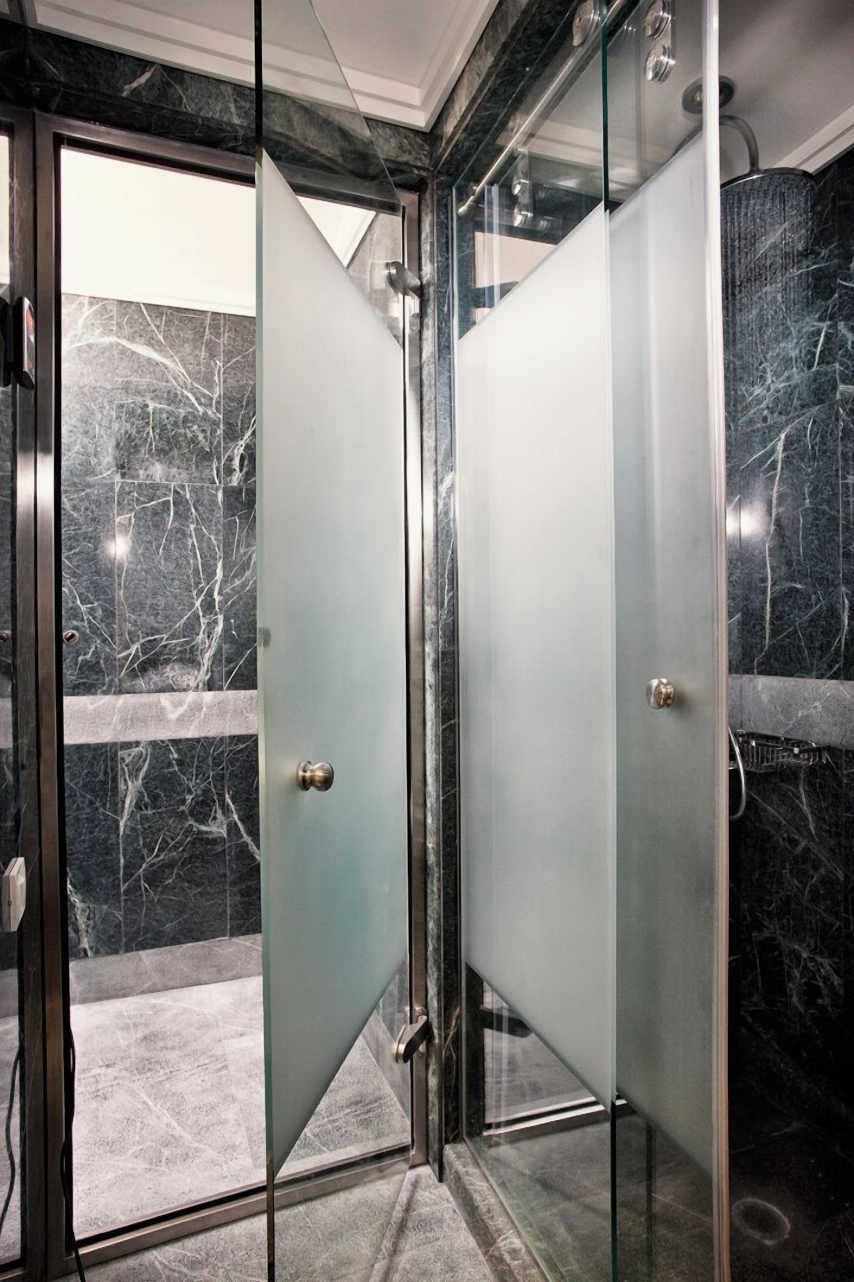 A modern bathroom with glass doors, marble walls, and a shower area.