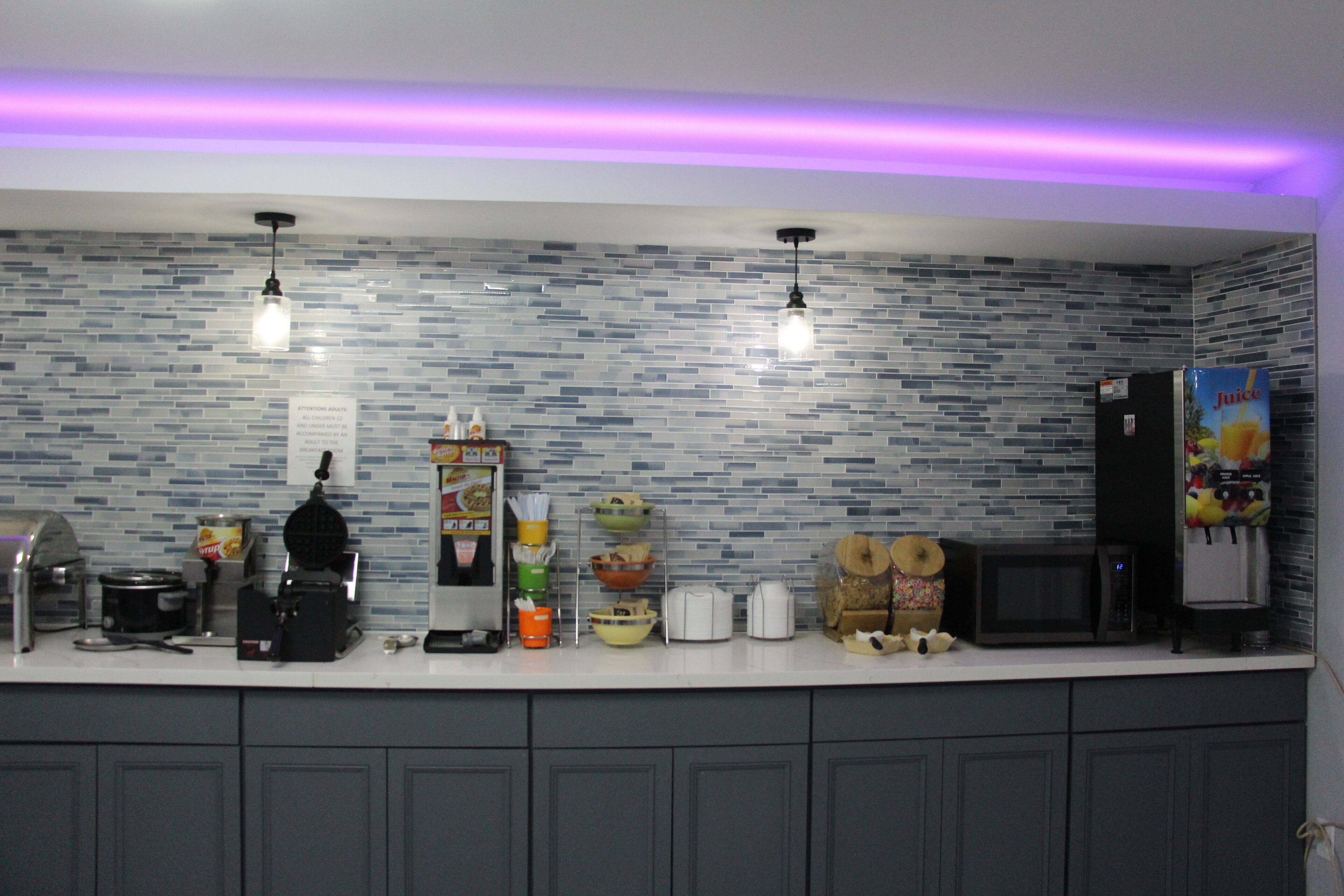 A kitchen with a tiled backsplash, a coffee machine, a microwave, and a refrigerator.
