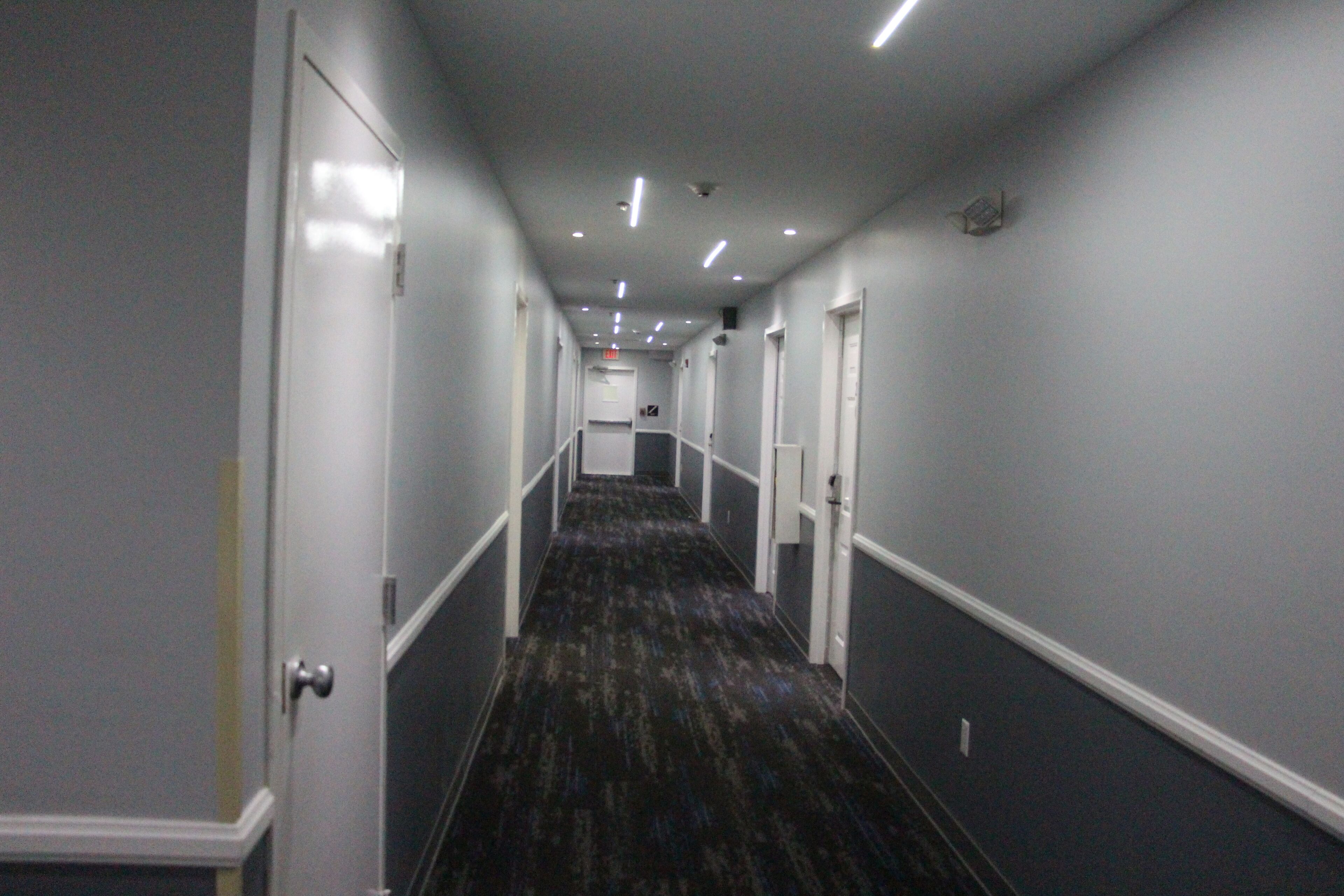 A narrow hallway with a carpeted floor, white walls, and doors on both sides.