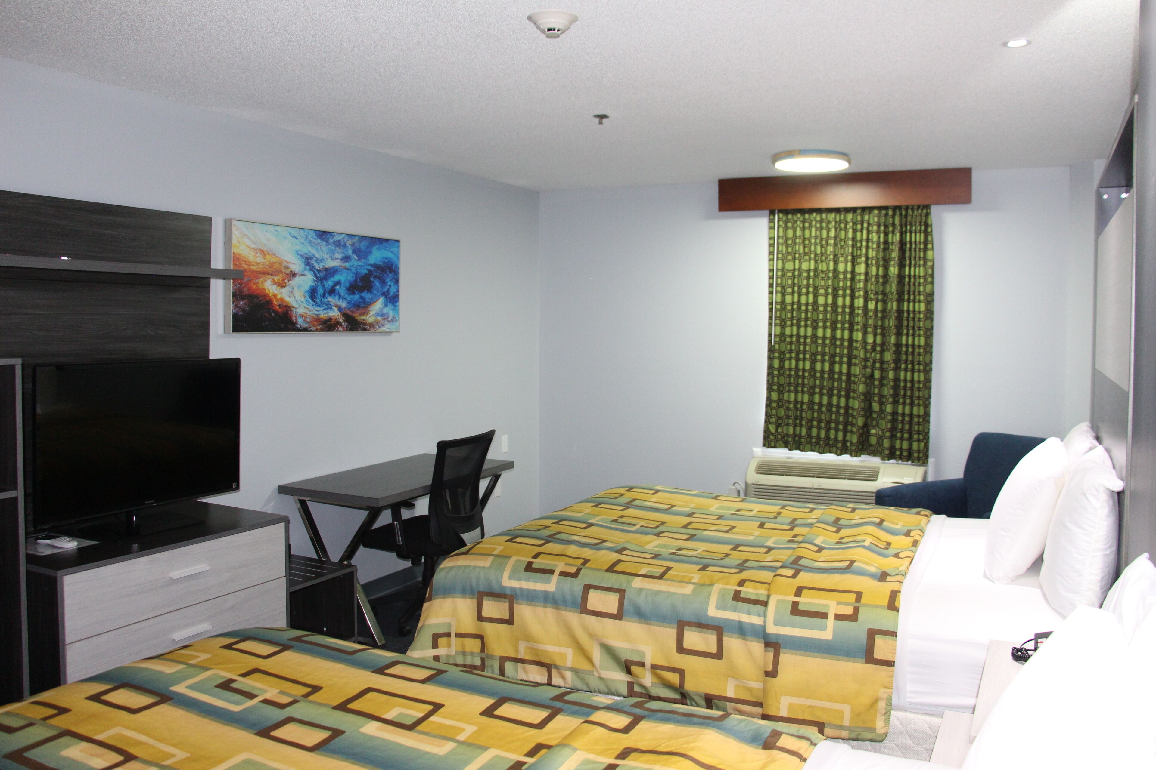 A hotel room with two beds, a desk, a chair, a television, and a window with curtains.