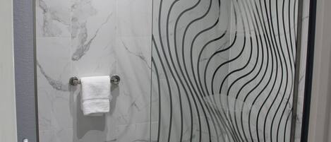 Un baño moderno con cabina de ducha de vidrio, pared con azulejos de mármol y un inodoro.