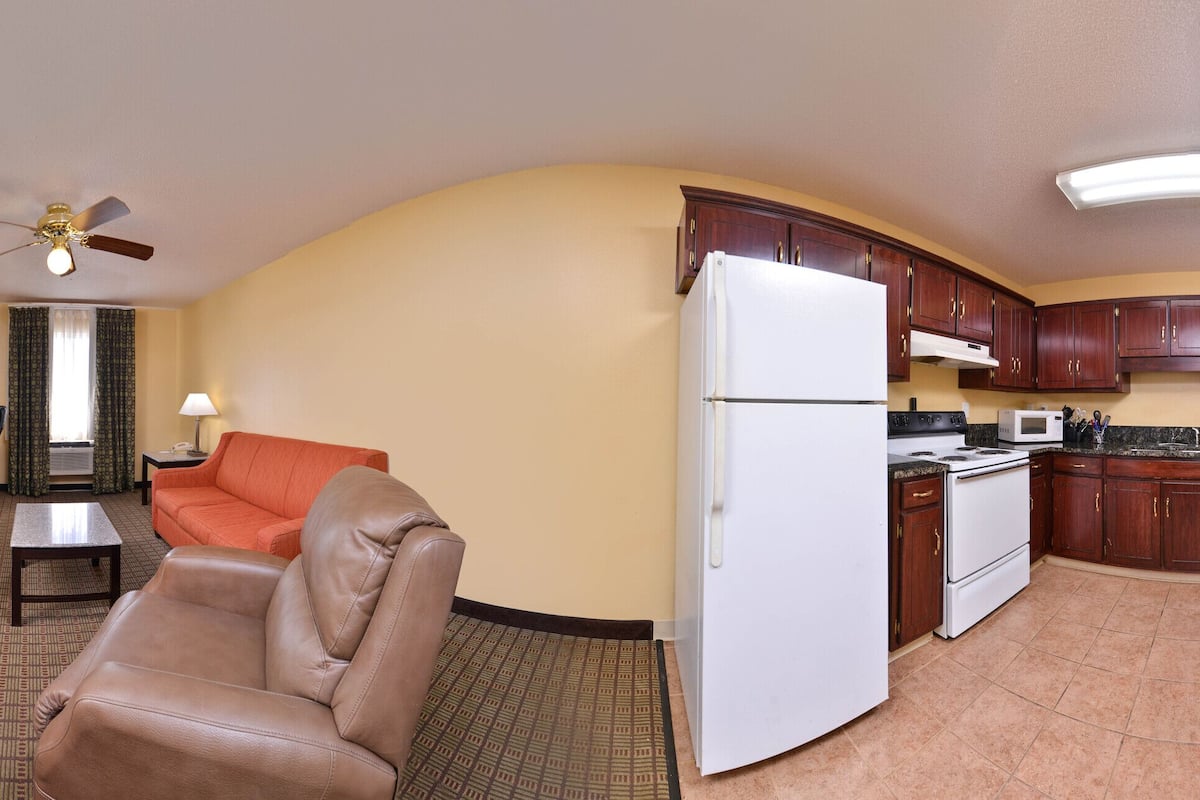 A compact hotel room with a dining area, kitchenette, and a living space with a sofa and armchair.