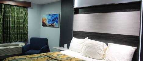 A hotel room with a bed, a chair, a painting, and a window with curtains.