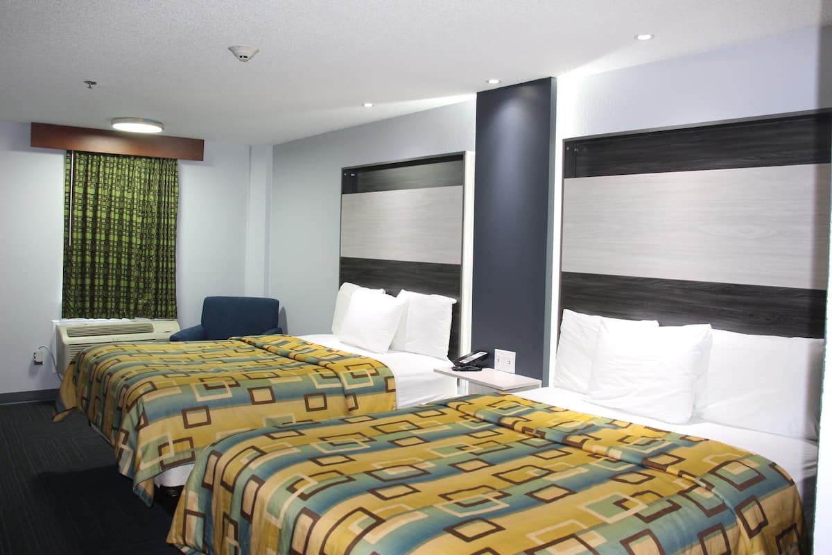 A hotel room with two beds, a desk, a chair, an air conditioning unit, and a window with curtains.