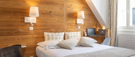 Un dormitorio con pared de madera, una cama con ropa de cama blanca, dos lámparas de noche, una silla y un escritorio con lámpara.