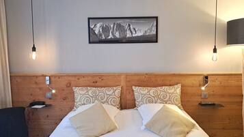 A hotel room with a wooden headboard, two patterned pillows, a framed mountain landscape picture, and bedside lamps.