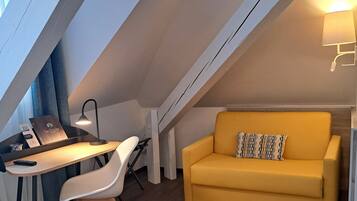 Ein gemütliches Schlafzimmer im Loft-Stil mit Schrägwand, einem Holztisch und einem gelben Sofa.