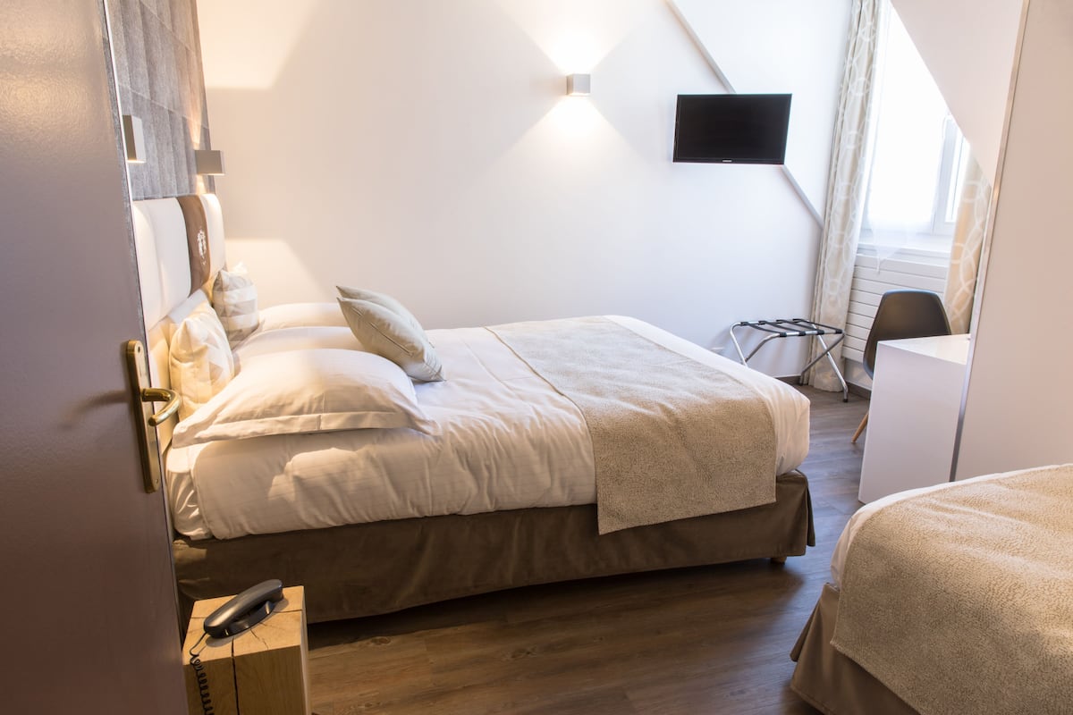 A hotel room with a bed, bedside table, and a TV mounted on the wall.