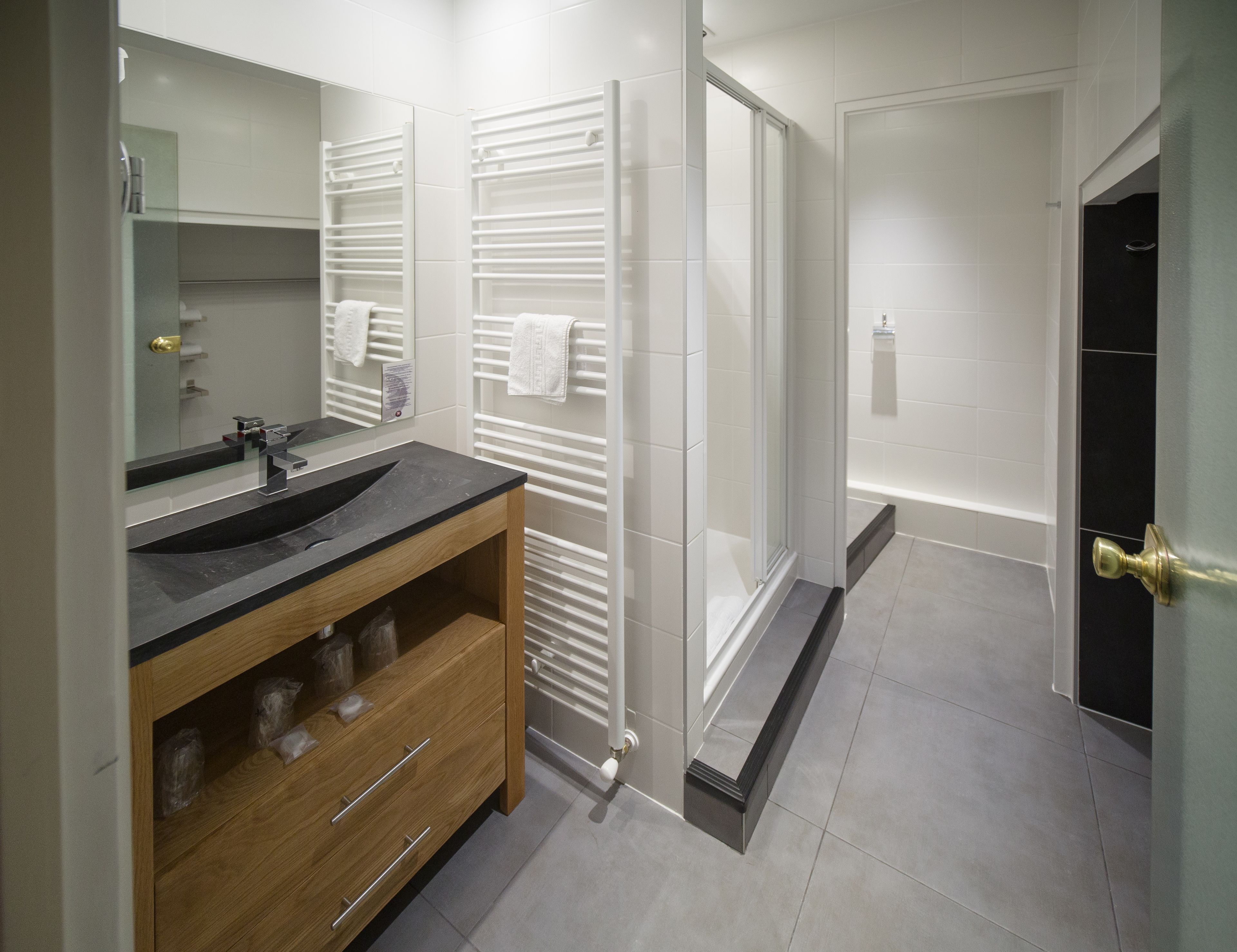 A modern bathroom with a large mirror, two sinks, a wooden vanity, a glass shower enclosure, and a bathtub.