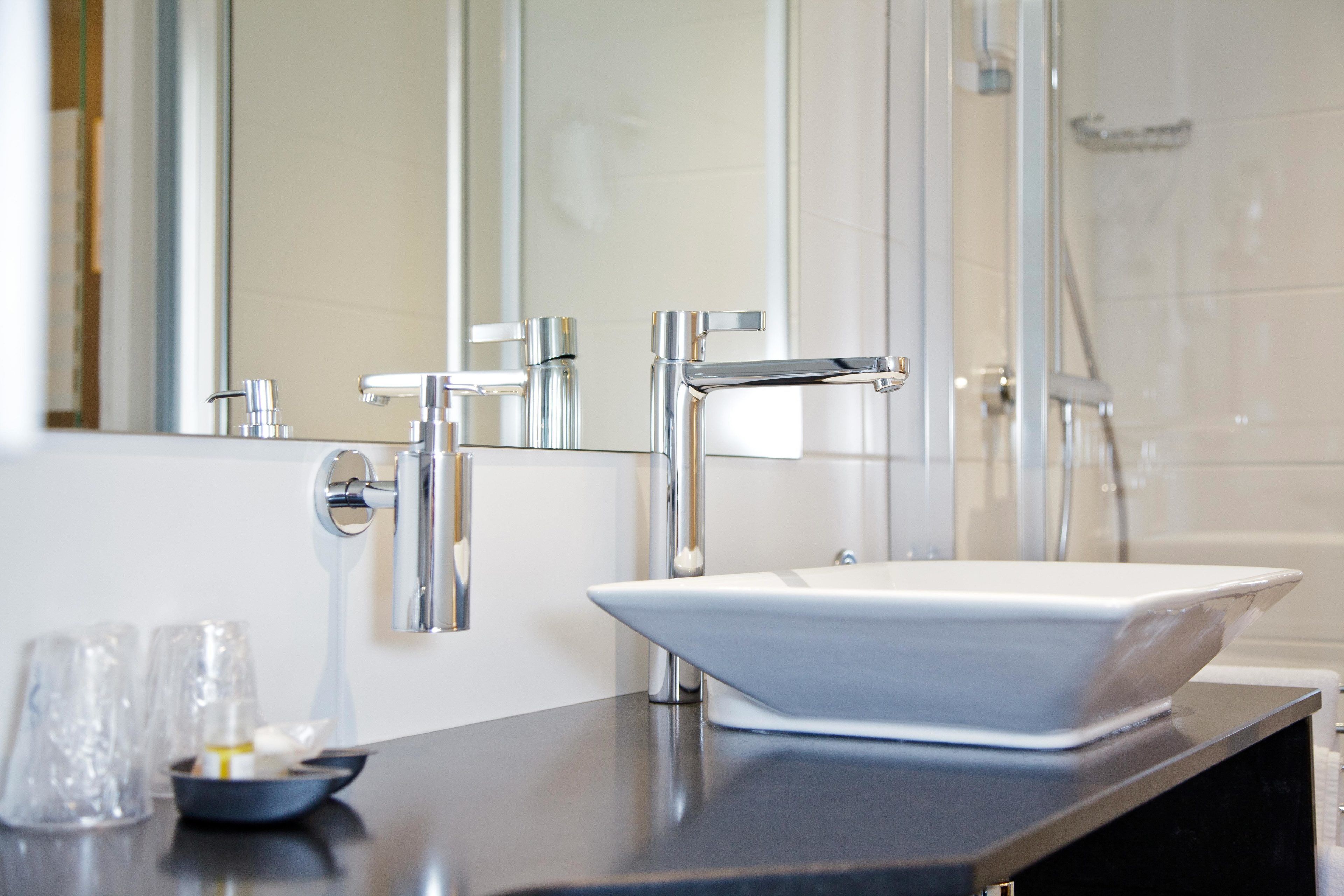 A modern bathroom with a large mirror, chrome fixtures, and a white sink.