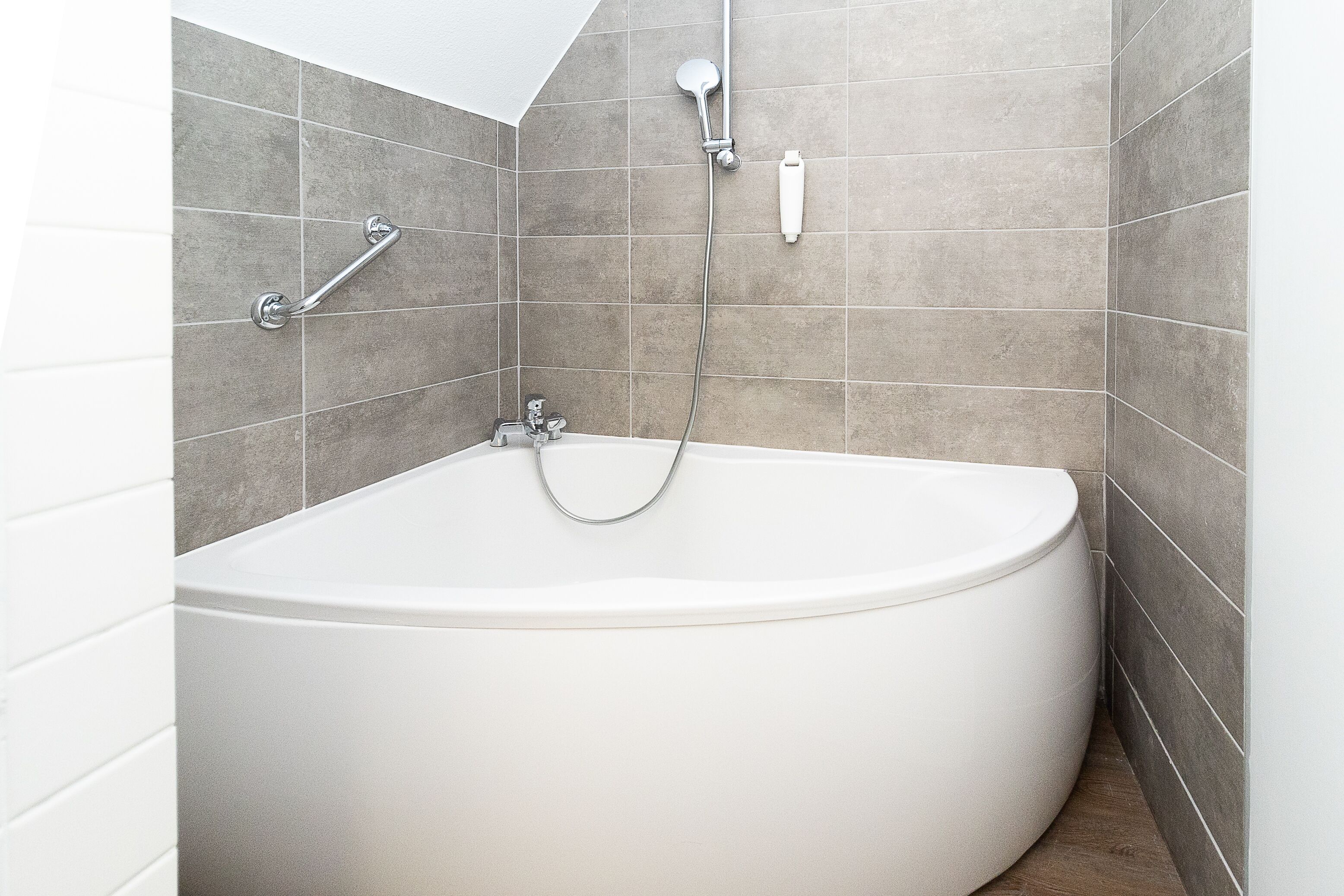 Un baño moderno con una bañera independiente, un cabezal de ducha manual y una barra de ducha manual.