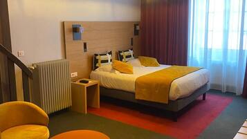 Quarto de hotel com uma cama, duas cadeiras, uma mesinha e um radiador.