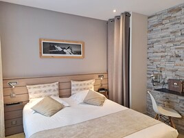 Un dormitorio ordenado con cama, almohadas, una mesita de noche, un escritorio con silla, una lámpara y un cuadro en la pared.