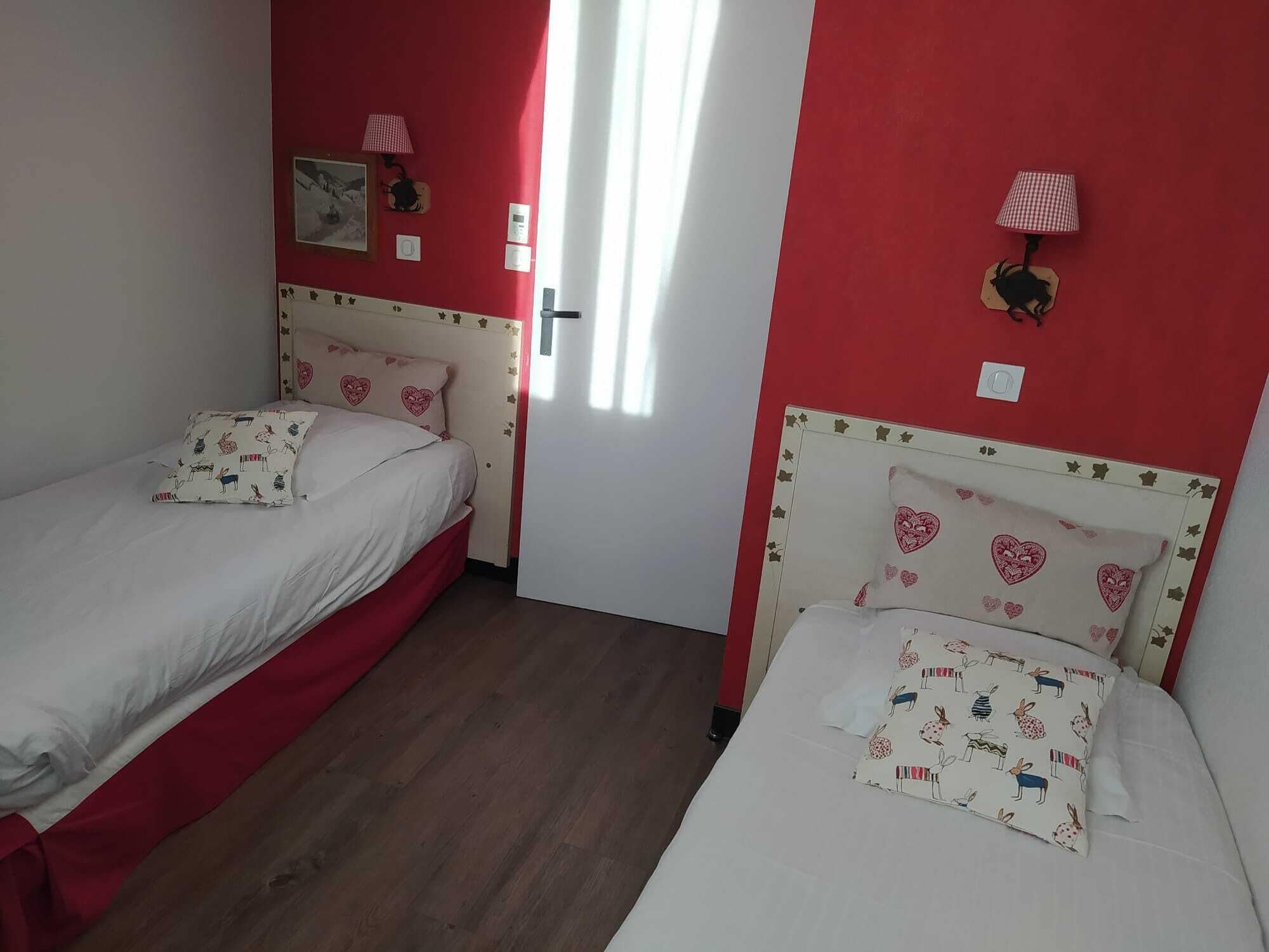 Une chambre avec deux lits simples, chacun agrémenté d’oreillers à motifs de cœur et un mur rouge.