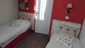 Une chambre avec deux lits simples, chacun agrémenté d’oreillers à motifs de cœur et un mur rouge.