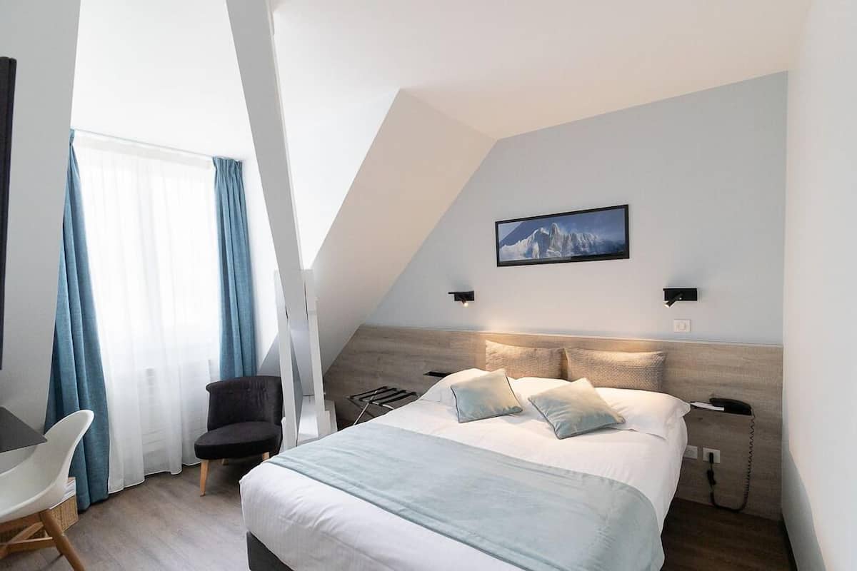 A modern hotel room with a bed, a desk, a chair, and a window with curtains.
