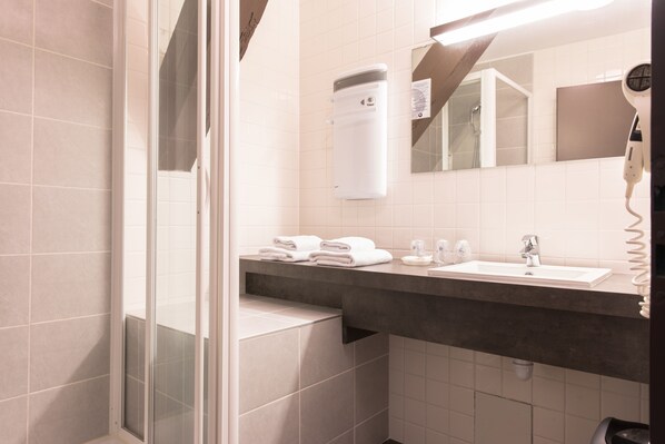 A bathroom with a glass shower enclosure, a white sink, a hairdryer, and neatly folded towels on the counter.