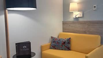 A modern room with a yellow sofa, a standing floor lamp, a small table with a book, and a wall-mounted air conditioner.