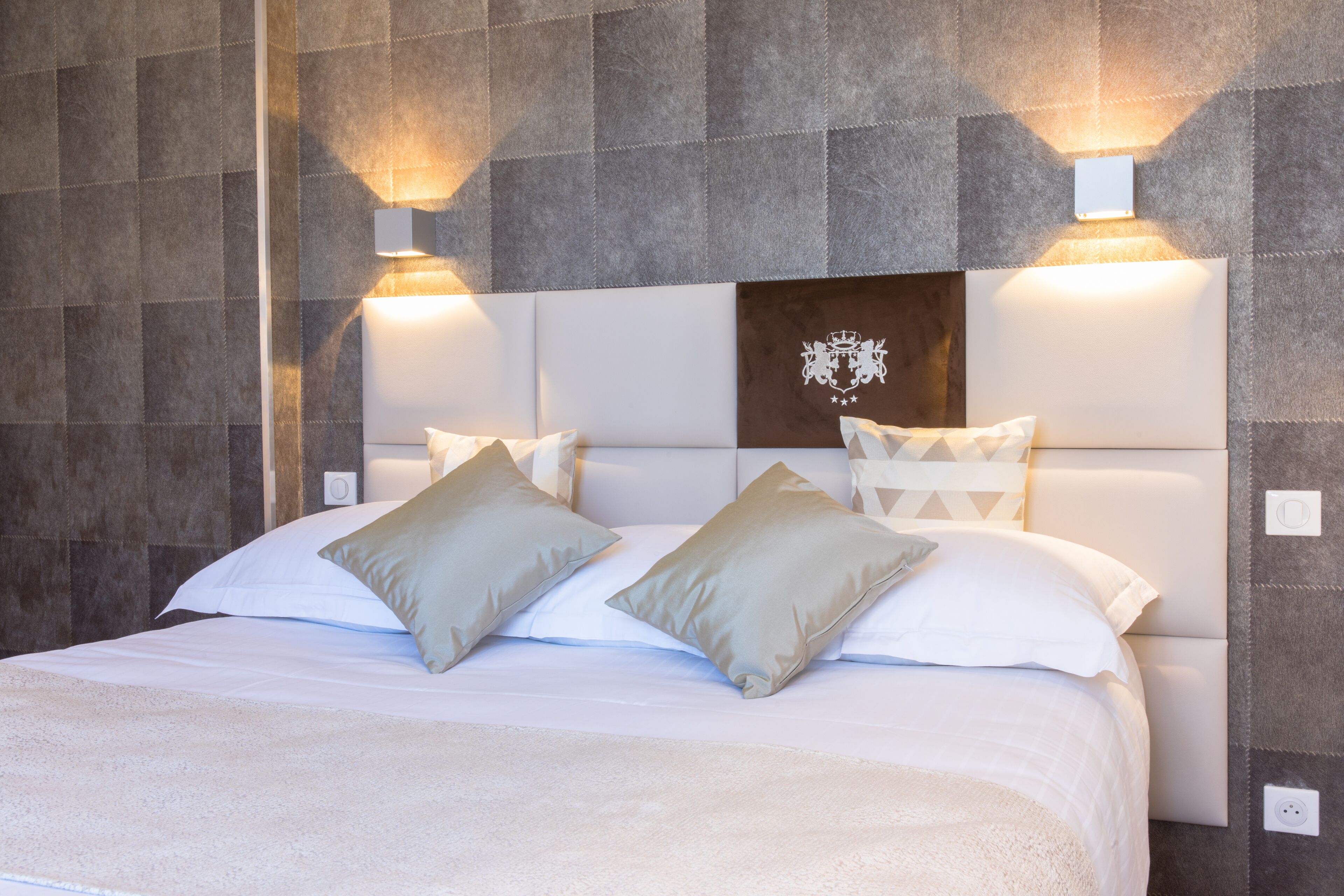 A modern hotel room with a large bed, two wall-mounted lights, and a decorative headboard.